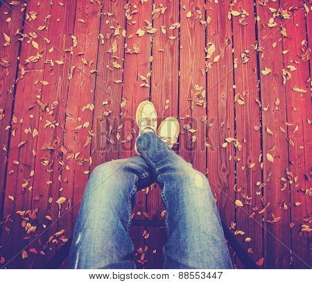 a pair of legs taken from overhead on a deck with leaves that have fallen toned with a retro vintage instagram filter app or action 