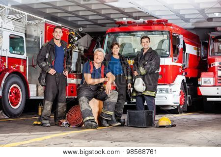 Portrait of happy firefighter's team with equipment against trucks at fire station