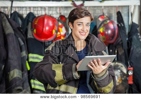 Portrait of happy firewoman in uniform holding digital tablet at fire station