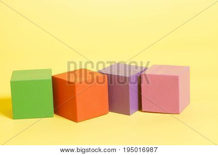Coloured wooden cubes on yellow background .