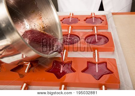 Sweets artisanal production of fruits loly pop at the factory. Close up of the saucepan pan with liquid hot red sugar dispensing to the orange mold. Artisanal production in France