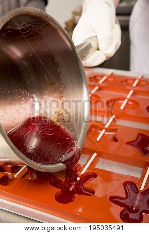 Sweets artisanal production of fruits loly pop at the factory. Close up of the saucepan pan with liquid hot red sugar dispensing to the orange mold. Artisanal production in France