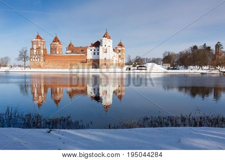 Mir Castle in Minsk region is ancient heritage of Belarus reflected in lake. UNESCO World Heritage. Winter scene with snow.