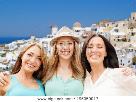 travel, tourism and summer vacation concept - group of happy smiling women or friends over oia town on santorini island background