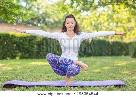 A slender girl is looking beautiful and athletic and doing physical exercise. A well-looking sports lady in a white sweater and leggings. A beautiful sportswoman issitting on one leg and spreading her hands to the sides.