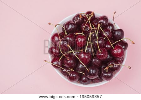 White Bowl Of Fresh Red Cherries On A Pink Background. Copy Space. Top View. Close-up