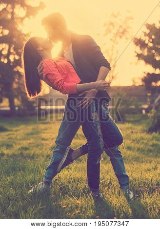 Dating couple of teenagers in the park at sunset. A girl and a boyfriend embrace and kiss. Love and happiness. Strong kiss. Frontal light of the setting sun.