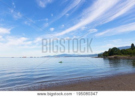 Sea landscape at the city beach in Vancouver Canada. Kayaking in the sea with ships in the roadstead and snow mountains on horizon.