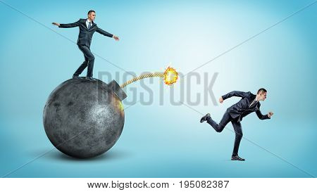 A businessman standing on a black round bomb with a lit fuse beside a man running away from it. Business competition. Drastic measures. Flee from trouble.