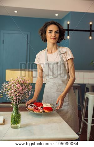 Portrait of a smiling young waitress in apron serving donuts on a tray in a caffeteria