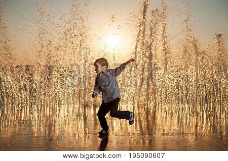 funny little amazed boy running away from high waves at the ocean sunset
