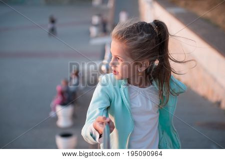 portrait of a beautiful little girl lit by warm sunset light wearing a turquoise blouse on the background of the town square