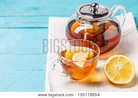 Glass cup of tea with lemon and glass teapot on blue wooden table.