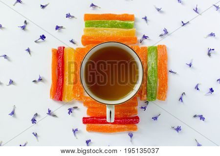 Cup of tea with pineapple candied fruits and small blue flowers on a white background