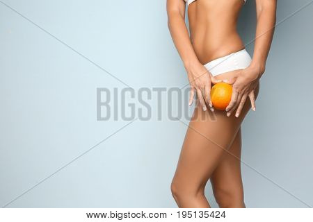 Young woman holding orange on light background. Cellulite problem concept