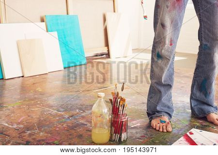 Low section of a male artist standing by paint brushes and paint thinner in studio