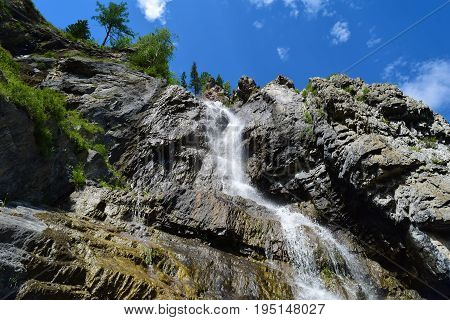 View of Shirlak waterfall in rocks on blue sky with white clouds background. Tektu river Altai Mountains Altay Republic Siberia Russia.