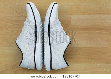 Top view side of white casual shoes with black lines on wooden background