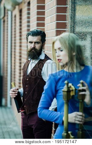 Hipster Holding Bottle Of Wine With Blurred Girl Opening Door