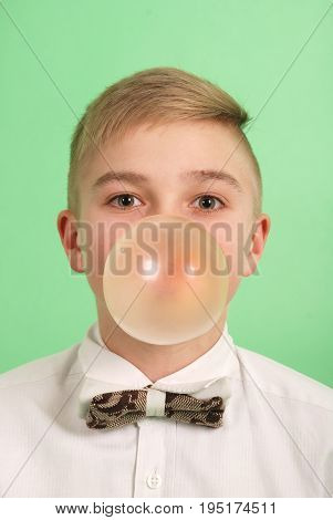 Boy blowing a bubblegum bubble isolated on green.