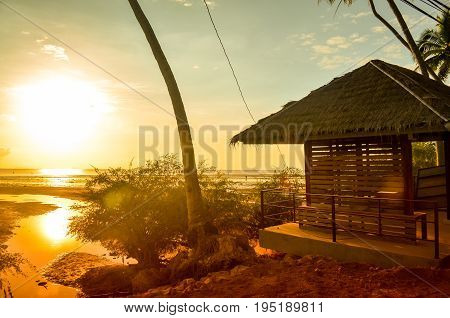 tropical sunset with wooden hut and palmtree at coast