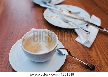 A dirty plate and an empty cup of coffee. Empty dishes after eating on a wooden table in a cafe.