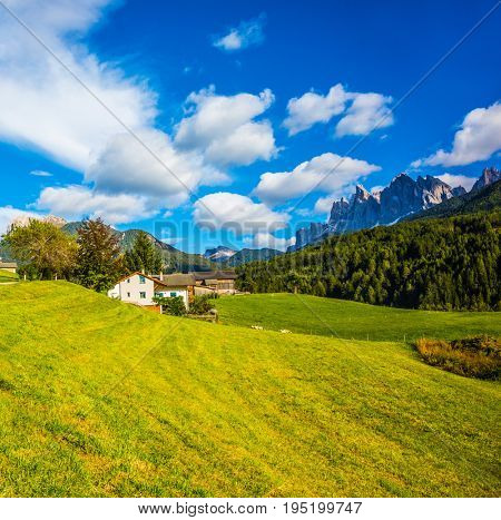 The valley is surrounded by a dentate wall of dolomite rocks. Charming chalet on a green grassy slope. Warm autumn in the Dolomites. The concept of ecological tourism