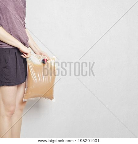 Girl holding plastic bag with tap full of apple juice, stucco wall background