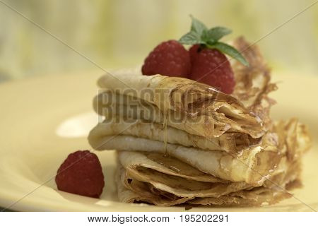 Serving French Crepes with fresh rasberries and honey on the plate. Close up.