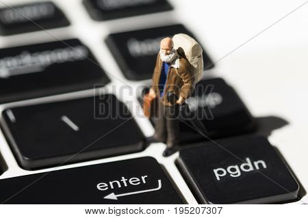 Tiny old traveler on white notebook keyboard with black buttons. Internet browsing or programming. Elder man computer education concept. Notebook keyboard closeup. Enter key close-up. Enter macrophoto