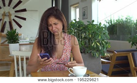 Woman can not make purchase with credit card on mobile phone. Female shopping online in cafe. Girl is sad and dissappointed because of failure. Unsuccessful payment.
