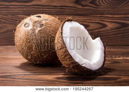 Close-up beautiful bright coconuts on a dark brown background. Delicious fresh cut in half coconut on a wooden table. Exotic tropical fruits. Vegan ingredients.