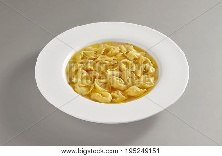 dish with portion of tortellini pasta in broth isolated on grey background