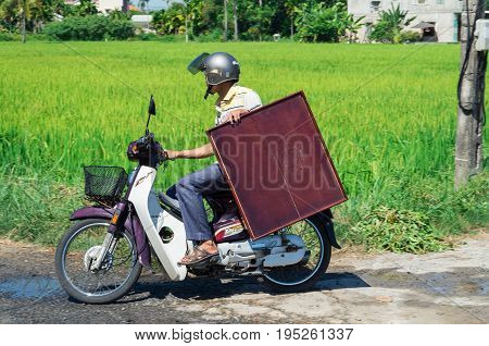 Hoi An - August 15, 2015: a Vietnamese man transporting a wooden table on a motorscooter.