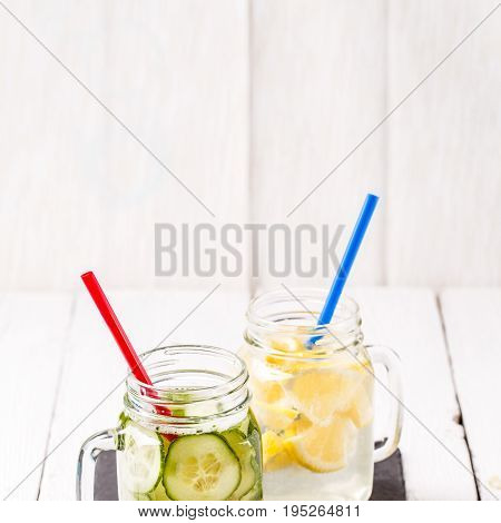 Two mugs of infused detox diet refreshing waters: with cucumber and lemon on white wooden table