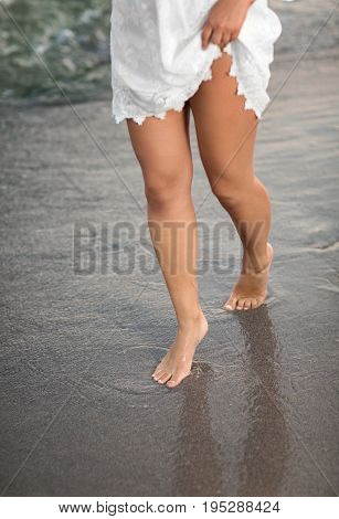 Female legs on a tropical blue sea and the sand beach. Pretty shapely legs on the shore of the ocean. Charming legs of a young woman in the sea and fine sand.