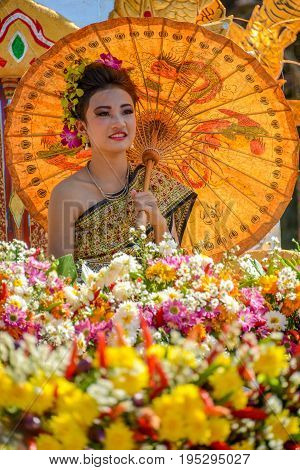 CHIANGMAI THAILAND - JANUARY 25 2015: Indigenous women and man with traitional costume sitting on decorated vehicle with flowers and bamboo hat fake elephants and chicken in parade of 22nd Traditional Skirt Fabric and The Indigenous Product and Culture Fe