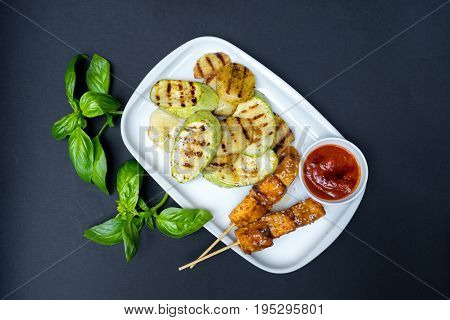 grilled tofu kebab on a white plate. Black background. Fresh basil leaves