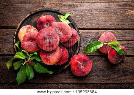 Peaches with leaves on wooden board, top view