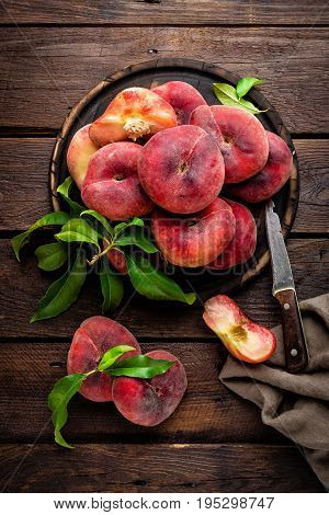 Peaches with leaves on wooden board, top view
