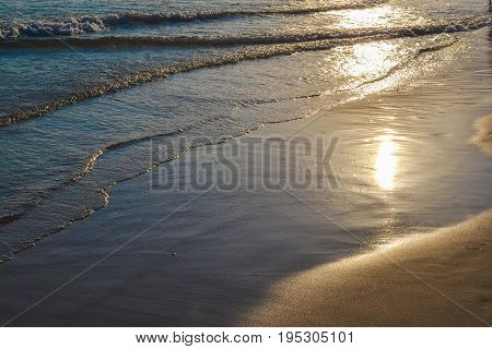 Evening calm waves in the sand. The sun is reflected in the water.