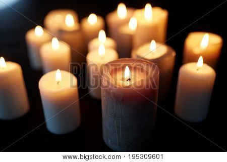 mourning and commemoration concept - candles burning in darkness over black background