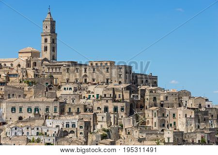 Old houses and a church in ancient architecture in the same kind of stone in a town built upon a hill known as the Sassi di Matera in Basilicata Italy.