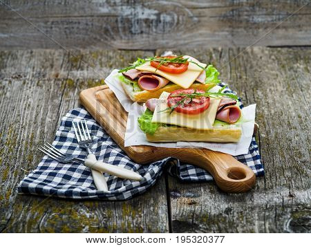 Sandwich with ham, cheese, olive oil and tomato on wooden board and on table