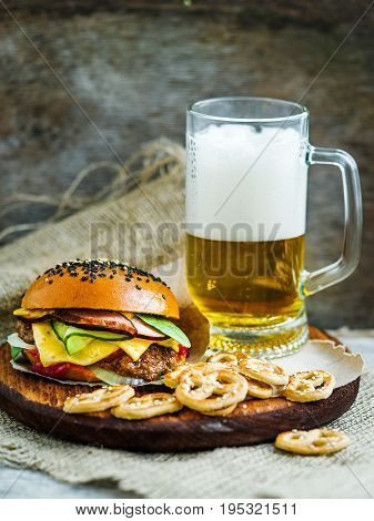 Tasty fresh hamburger with glass of beer and marinated cucumbers on wooden board