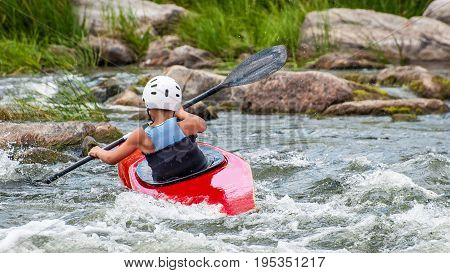 A teenager trains in the art of kayaking. Slalom boats on rough river rapids. The child is skillfully engaged in rafting.