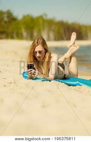 Summertime pleasures enjoying vacation concept. Woman in bikini sunbathing and relaxing on beach using smartphone checking social media and writing sms
