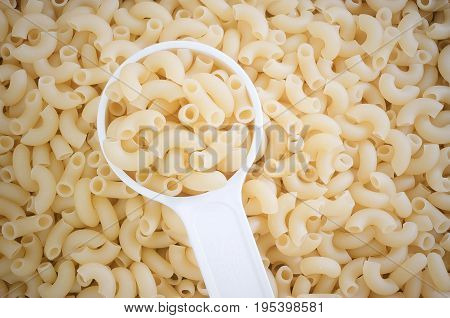 Food and Cuisine Top View of Uncooked and Dried Elbow Macaroni or Gomiti Pasta in Plastic Measuring Cup.