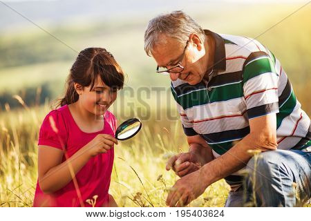 Happy grandfather and granddaughter explore together with magnifying glass nature.