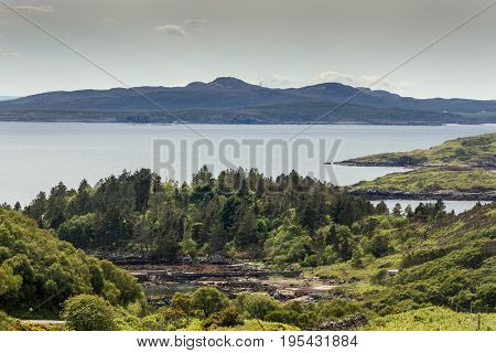 Assynt Peninsula Scotland - June 7 2012: Green rough hilly forested shoreline of Atlantic Ocean inlet near Loch An Arbhair with mountains on horizon.
